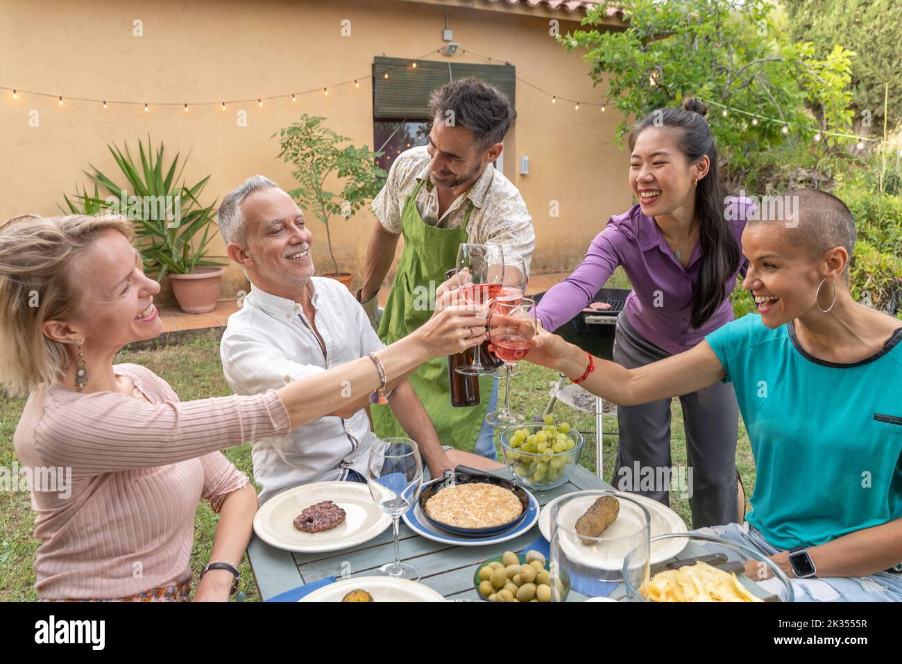 Un groupe d'amis qui toasque avec un grand sourire autour de la table au restaurant sur le patio de la maison. Banque D'Images