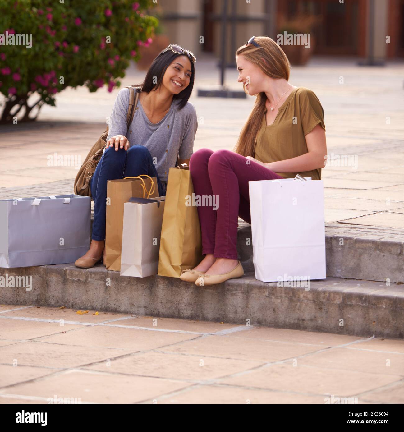 Faites vos courses jusqu'à épuisement. Deux jeunes femmes discutant sur les marches après une longue et réussie journée de shopping. Banque D'Images
