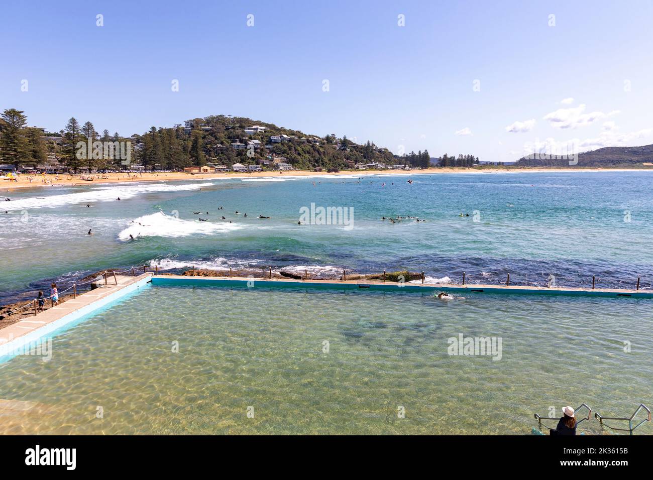 Palm Beach Sydney avec des surfeurs dans l'océan et une dame assis à côté de la piscine de roche de l'océan piscine construite dans les années 1920, Sydney, NSW, Australie Banque D'Images