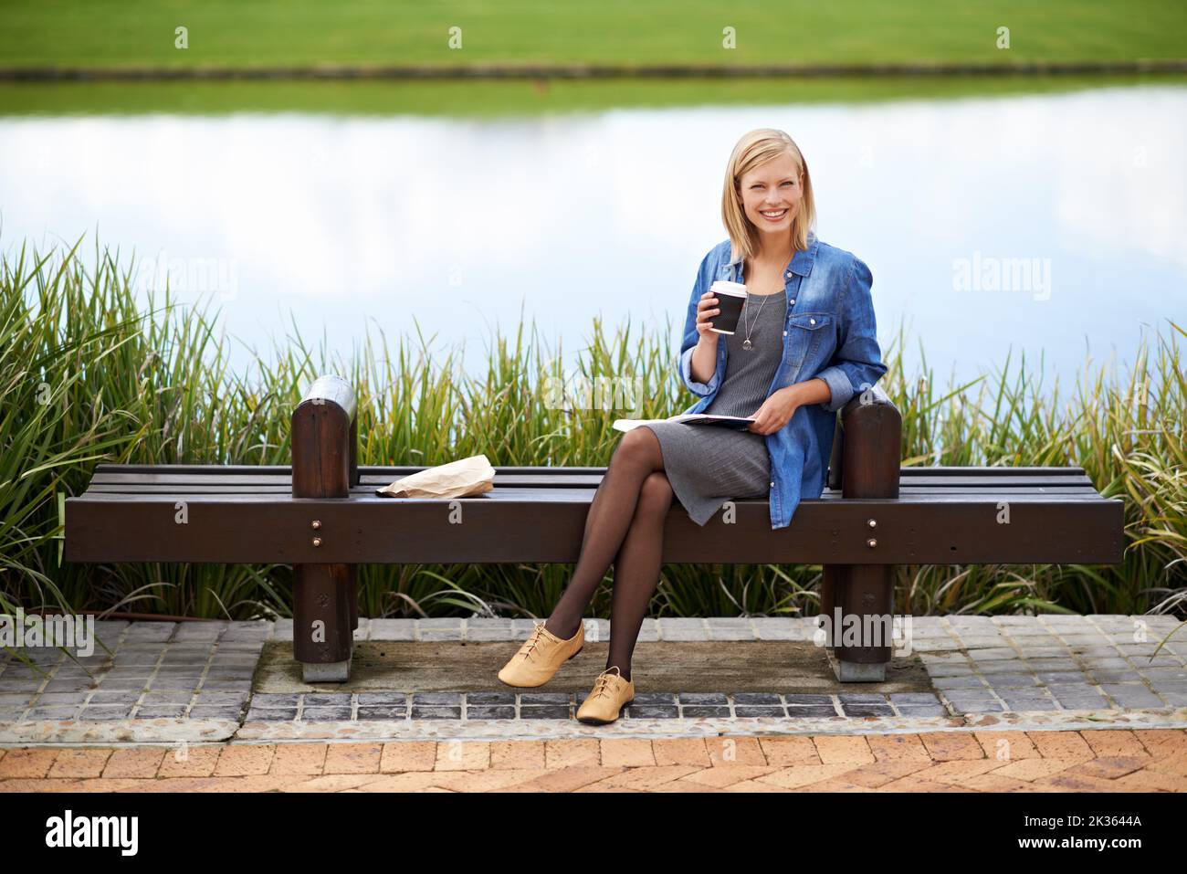 Faire compter son heure de déjeuner. Une jolie femme blonde lisant un livre pendant sa pause déjeuner sur un banc de parc. Banque D'Images