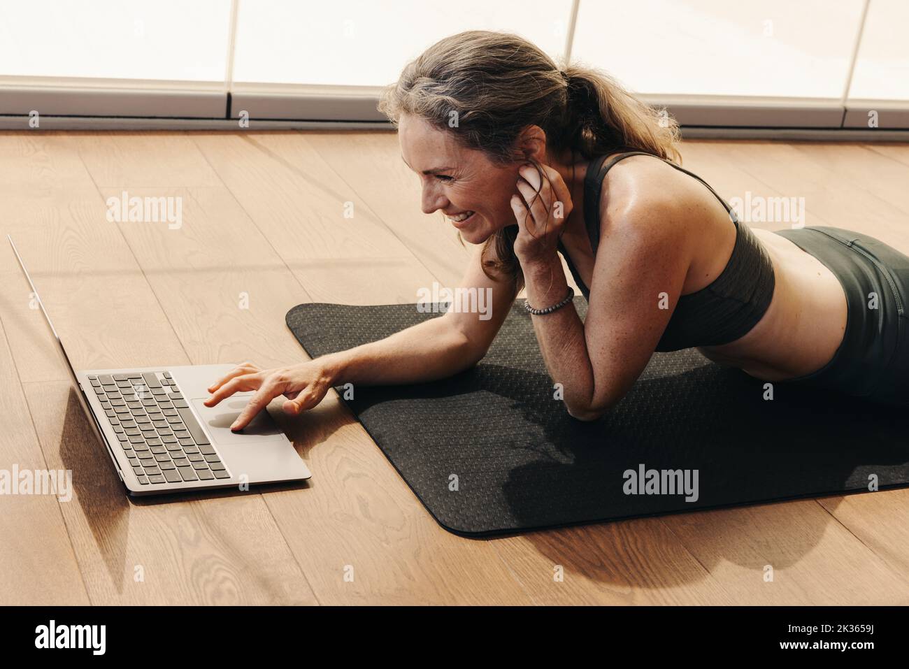 Femme âgée souriant tout en participant à un cours de fitness en ligne sur un ordinateur portable. Bonne femme suivant un tutoriel de yoga en ligne à la maison. Femme âgée gaie l Banque D'Images