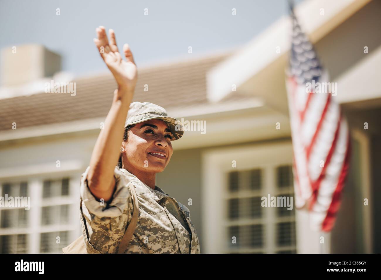 Une femme patriotique sourit et agite fièrement sa main en se tenant à l'extérieur de sa maison. Une militaire américaine rentre chez elle après l'avoir servi Banque D'Images