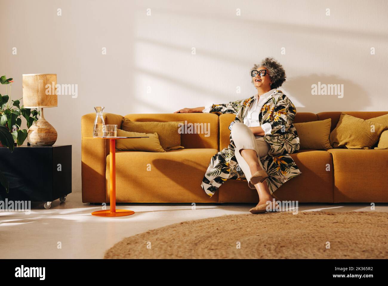 Femme d'affaires mûre souriant en s'asseyant sur un canapé dans le hall d'un bureau. Femme d'affaires gaie travaillant dans un bureau de collègue créatif. Banque D'Images