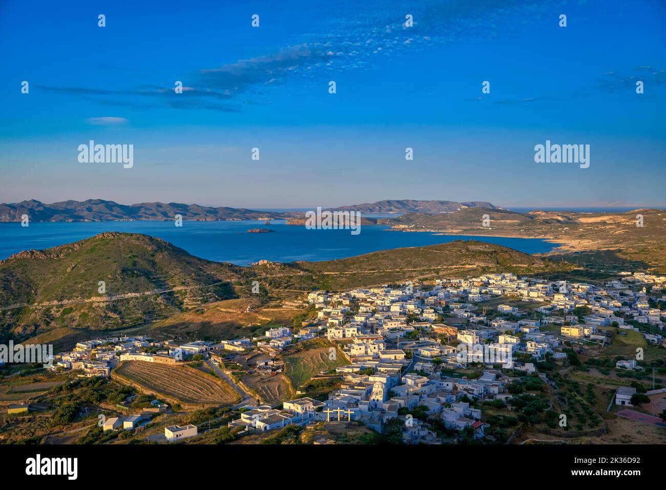 Belle vue sur la ville grecque typique, la baie et les villages sur l'île au coucher du soleil, Grèce. Maisons blanchies à la chaux, collines verdoyantes, soleil bas, mer bleue, ciel clair Banque D'Images