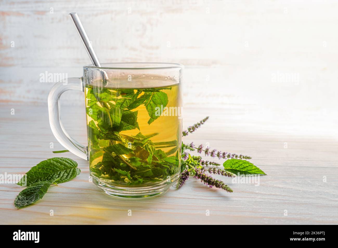 feuilles et fleurs de menthe poivrée fraîches brassées comme thé aux herbes dans une tasse de verre sur une table en bois clair, espace de copie, foyer sélectionné, profondeur de champ étroite Banque D'Images