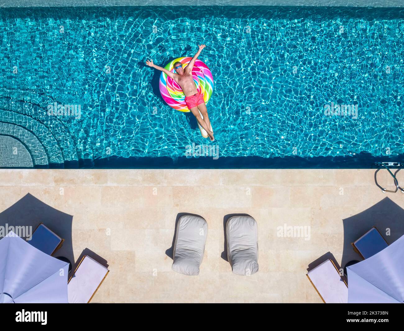 Vue aérienne d'un heureux homme flottant sur un jouet gonflable dans une piscine Banque D'Images