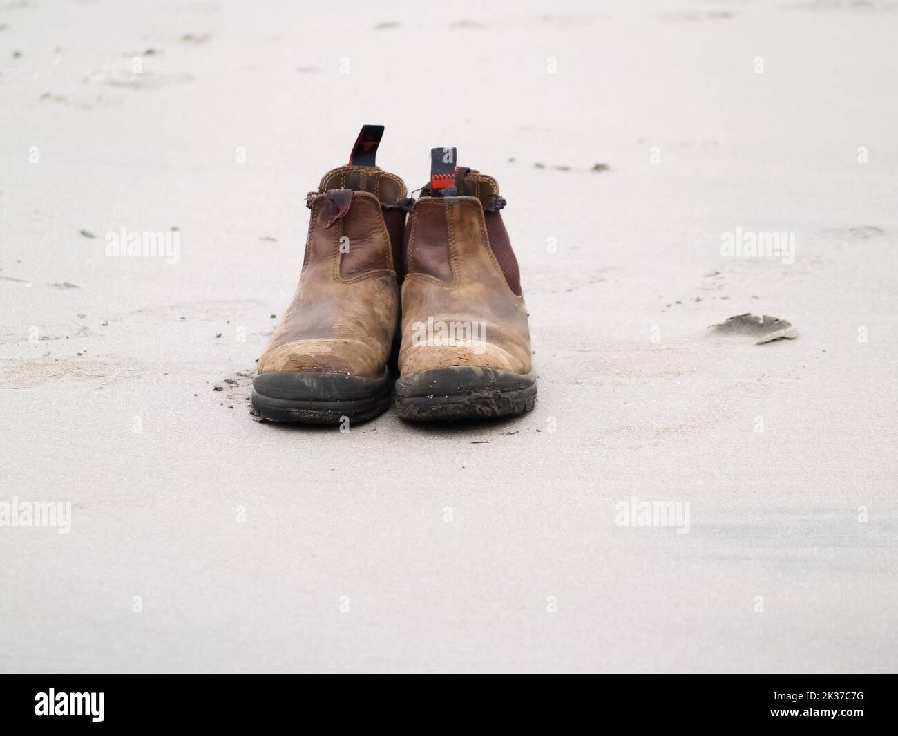 Associez de vieilles bottes en cuir sur le sable de la plage. Banque D'Images