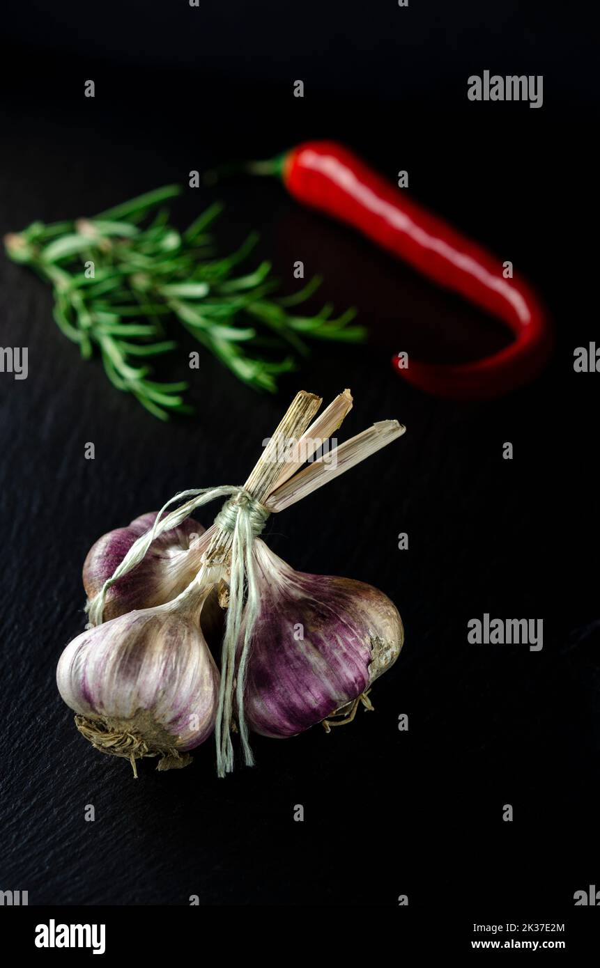 Épices pour la cuisine. Un bouquet d'ail sur fond noir à côté de la cormarine et des piments Banque D'Images