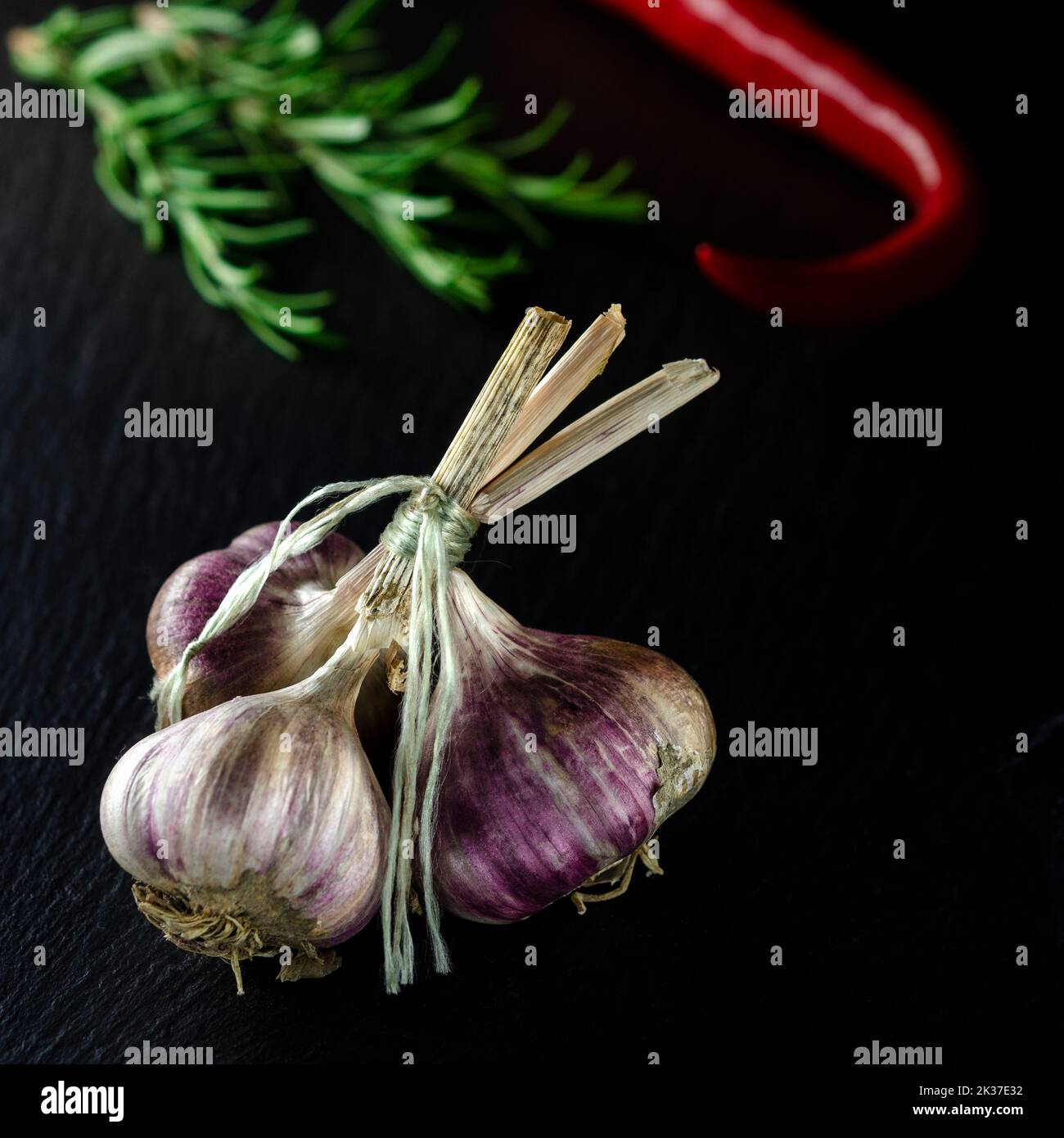 Épices pour la cuisine. Un bouquet d'ail sur fond noir à côté de la cormarine et des piments Banque D'Images