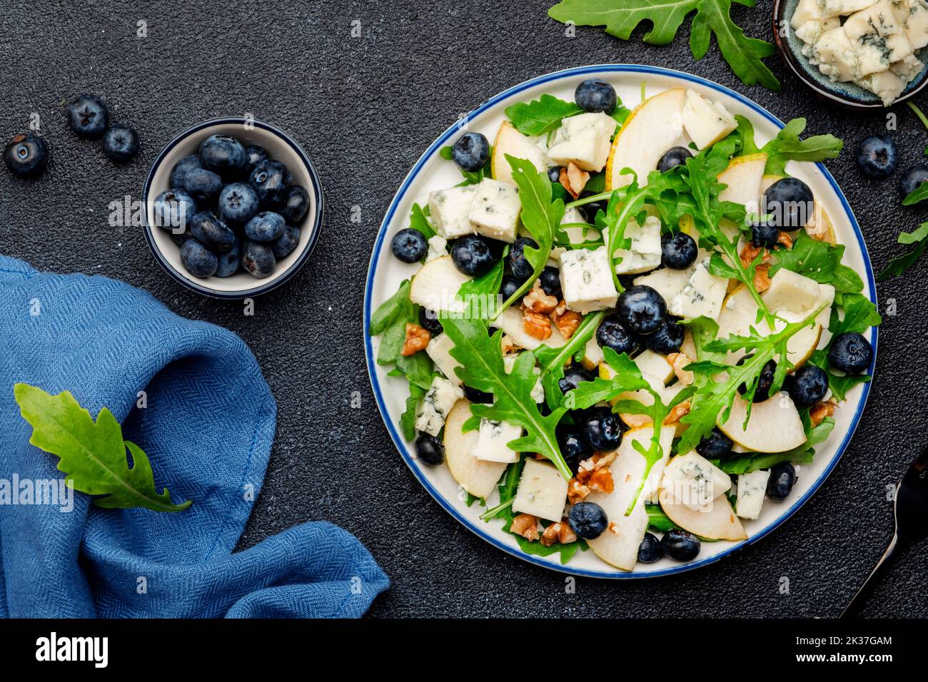 Delicious arugula salad with pears, blueberries, roquefort cheese and walnuts. Black kitchen table background, top view Banque D'Images