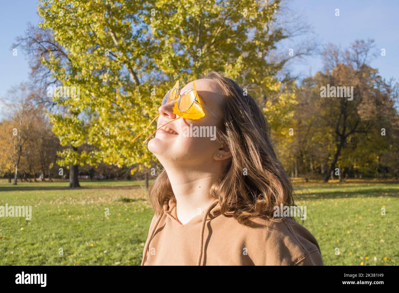 Portrait d'automne de jolie jeune femme avec des feuilles jaunes sous les lunettes. Regarder le soleil, sourire. Banque D'Images