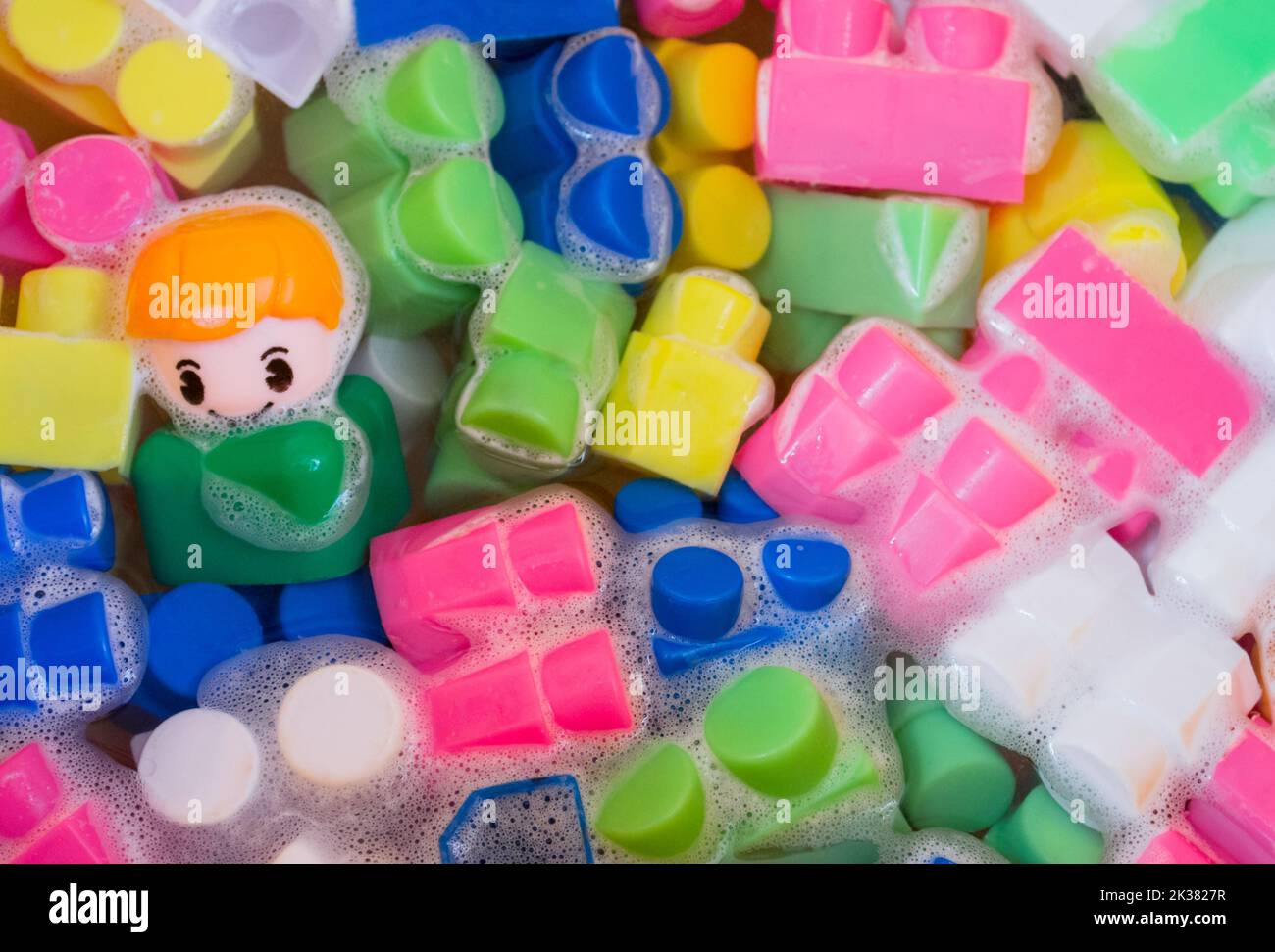 Lavage de jouets pour enfants, blocs de construction en plastique avec figurines. Un petit ami souriant et des cubes colorés flottent dans l'eau mousseuse. Le concept o Banque D'Images