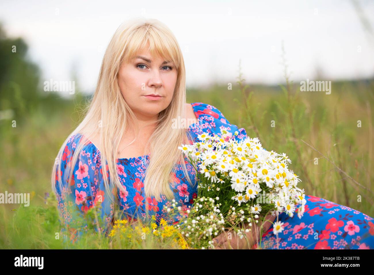 Une belle fille de taille plus avec des cheveux blancs dans une robe d'été pose sur la rue avec des pâquerettes. Chubby fille dans un pré avec des pâquerettes gros plan. Banque D'Images