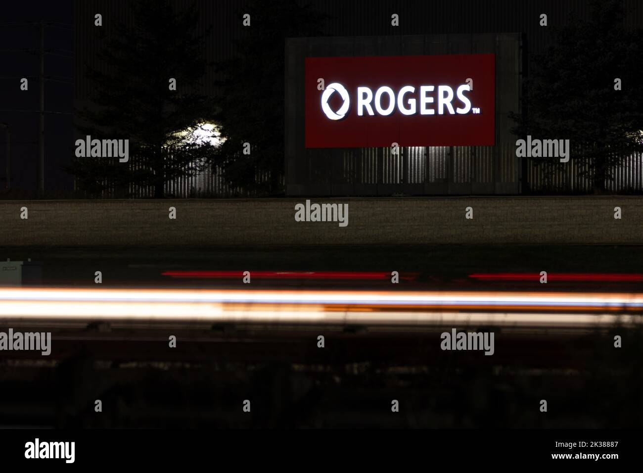 Le logo Rogers est illuminé sur un panneau, vu la nuit le long d'une autoroute très fréquentée; Rogers est le plus grand fournisseur de services sans fil au Canada et une entreprise de médias. Banque D'Images