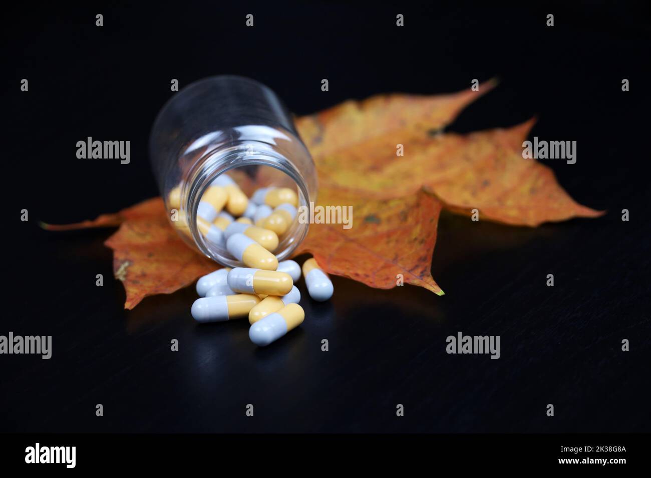 Pilules et feuille d'érable d'automne sur table en bois sombre, bouteille avec capsules dispersées. Pharmacie, antidépresseurs, vitamines pour l'immunité en saison de la grippe Banque D'Images