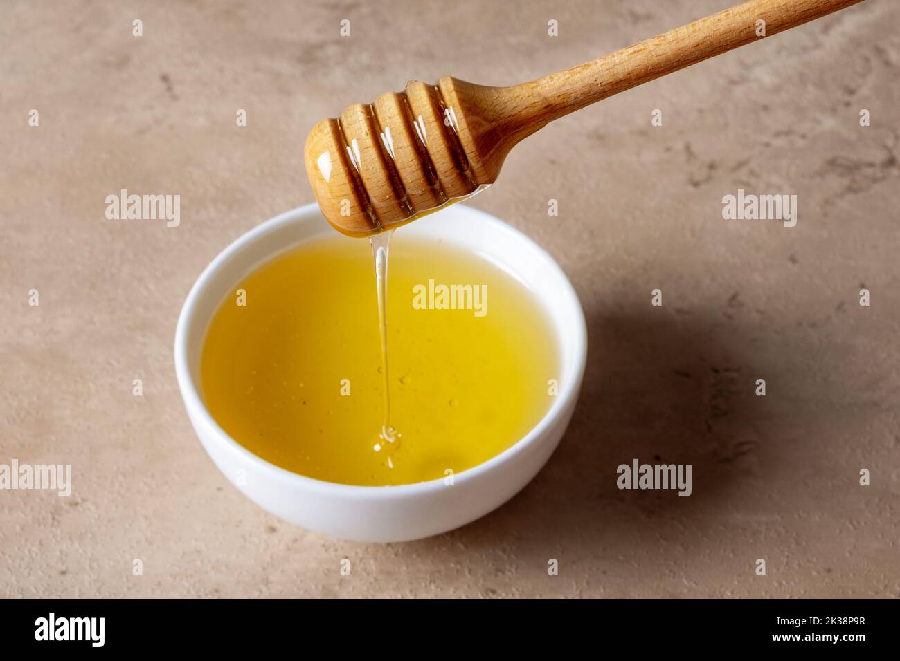 Un bol de miel et une cuillère en bois pour le miel sur une surface légère. Le miel liquide coule dans le bol. Mise au point sélective. Banque D'Images
