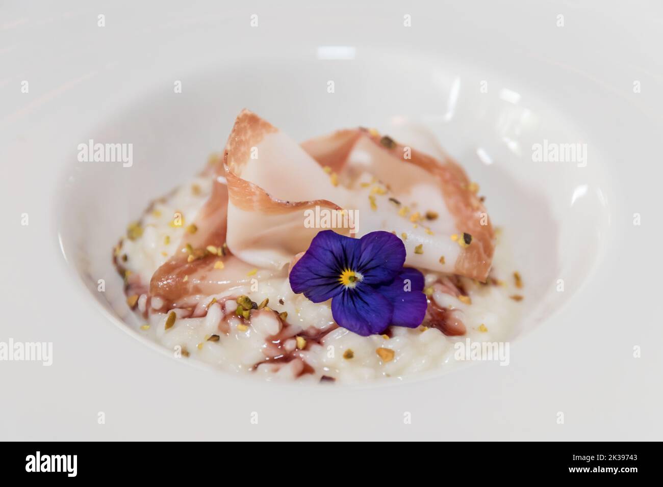 Risotto à la pistache et au bacon sur une assiette blanche, décoré de fleurs violettes. Banque D'Images