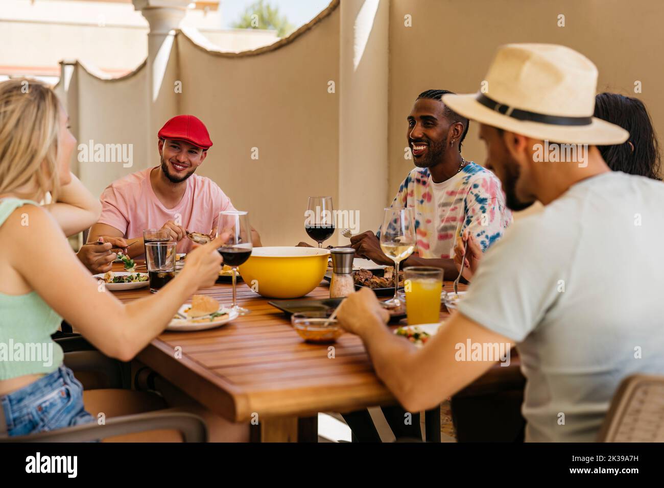 Un homme noir et un homme caucasien dans une casquette rouge écoutent avec des sourires pendant qu'ils célèbrent le déjeuner avec des amis. Banque D'Images