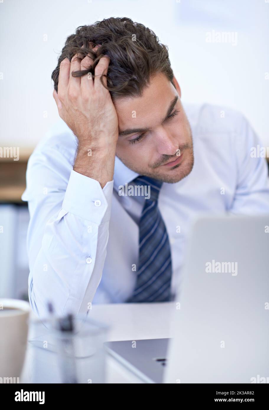 Trop de travail et pas assez de temps. Un jeune homme d'affaires semble frustré en étant assis à son bureau. Banque D'Images