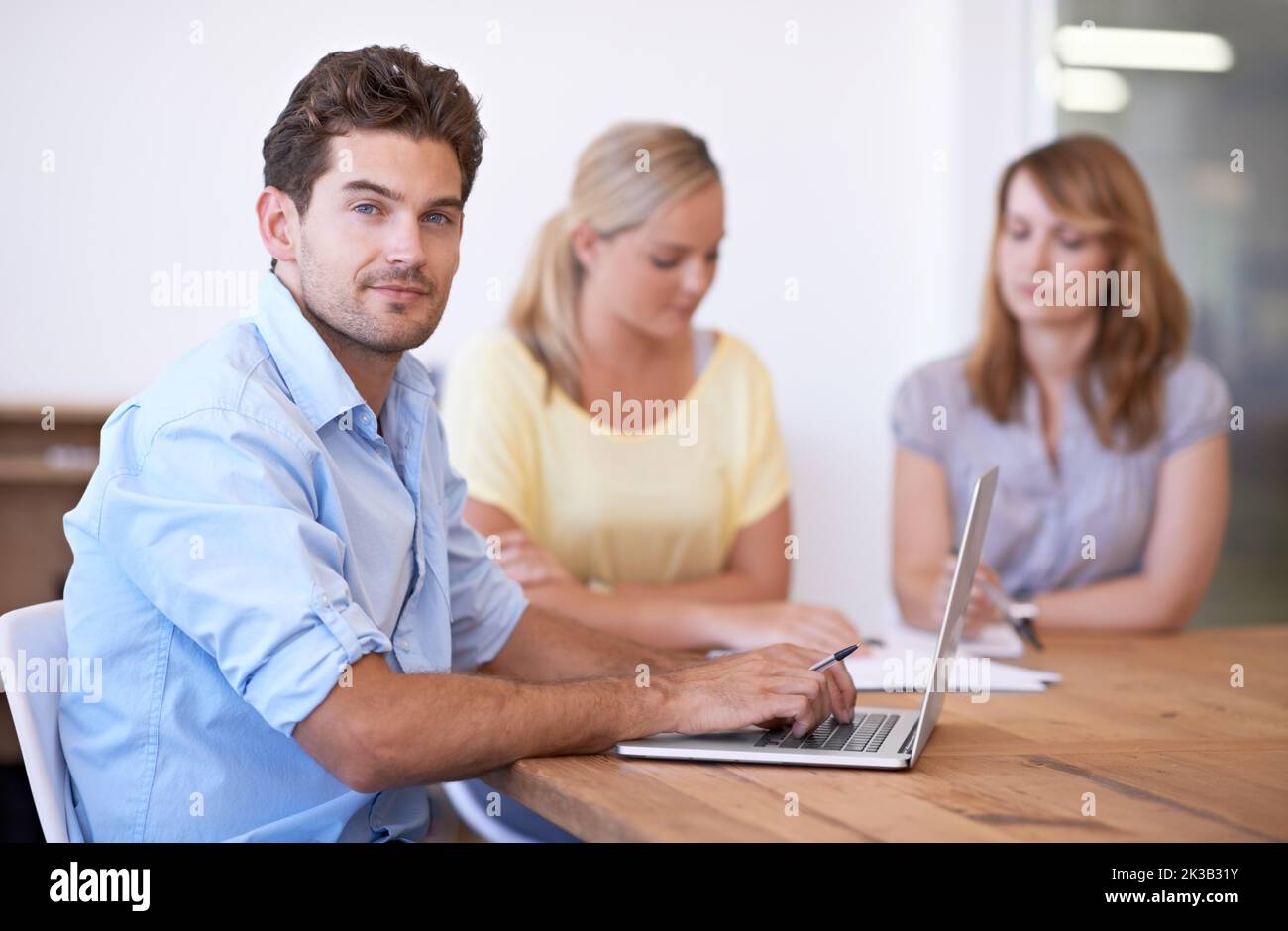 HES plein d'idées innovantes. Un jeune homme d'affaires assis avec un ordinateur portable et ses collègues en arrière-plan. Banque D'Images