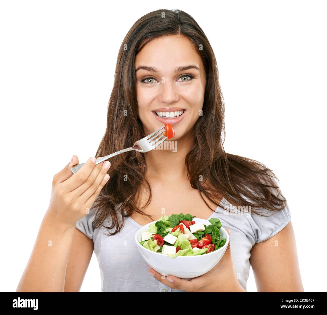 Un en-cas sain. Une jeune femme gaie mangeant une salade fraîche - isolée sur blanc. Banque D'Images