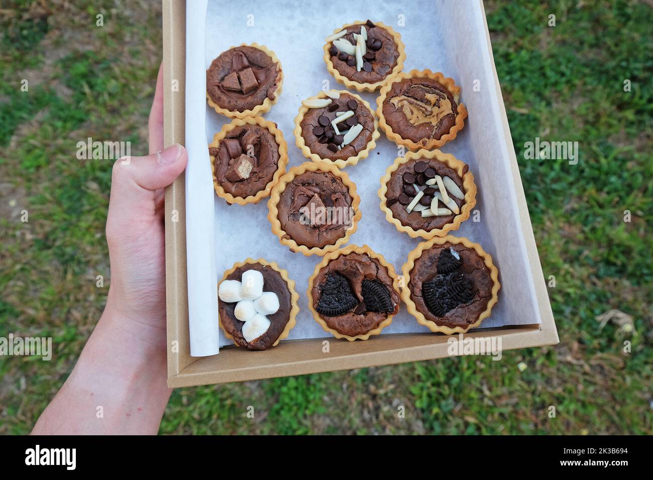 Boîte de papier en gros plan de tartes au brownie au caramel au chocolat recouverte de bâtonnets d'amande en tranches, de guimauve, de barre à sucre et de beurre d'arachide Banque D'Images