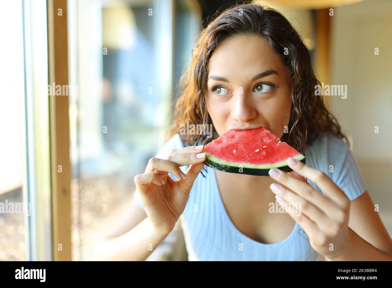 Femme dans un restaurant mangeant de pastèque regardant par une fenêtre Banque D'Images