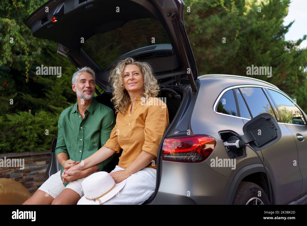 Couple d'âge moyen assis dans le coffre en attendant de charger la voiture avant de voyager pendant les vacances d'été. Banque D'Images