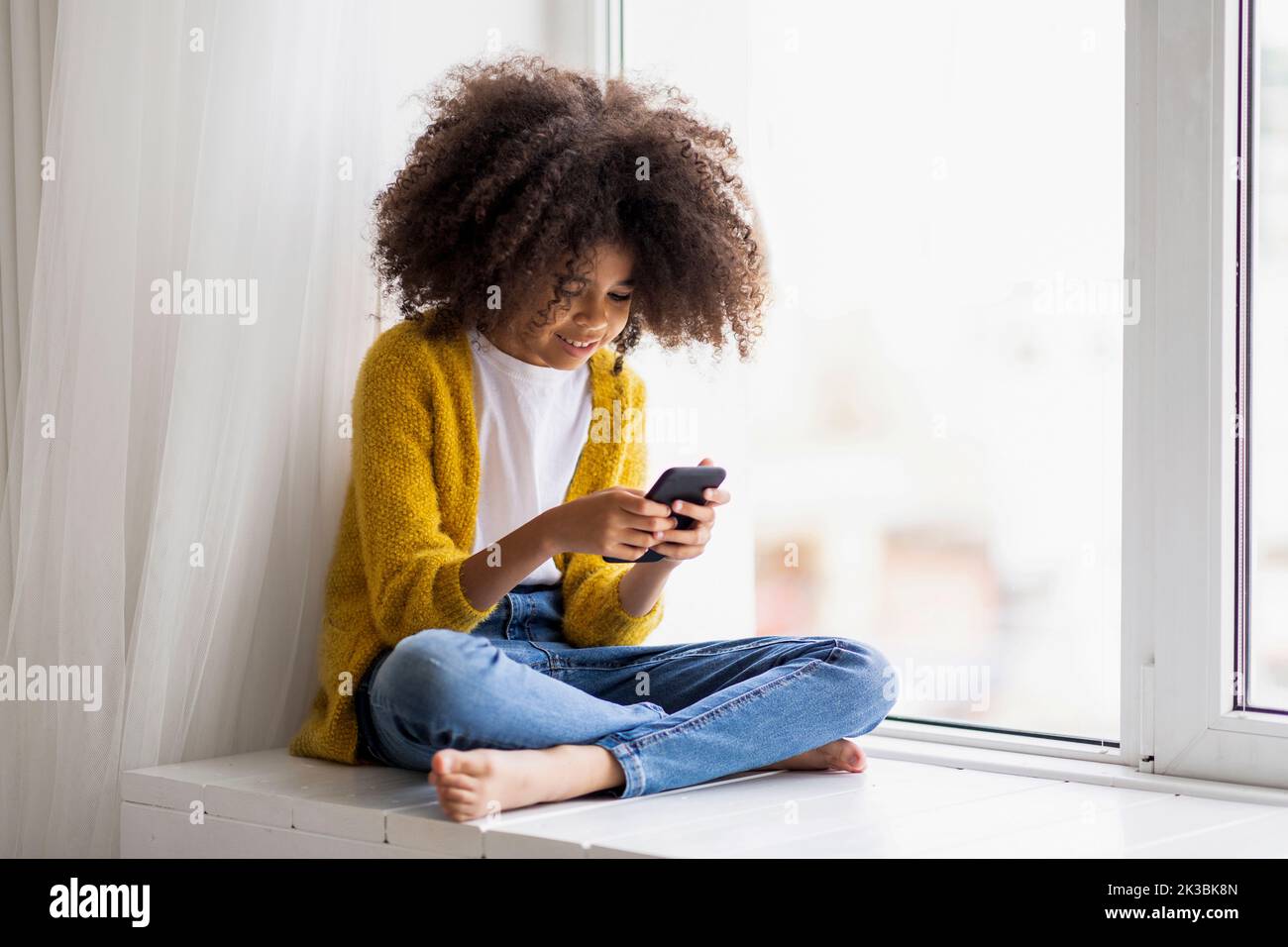 Enfant noir positif utilisant un téléphone cellulaire à la maison Banque D'Images