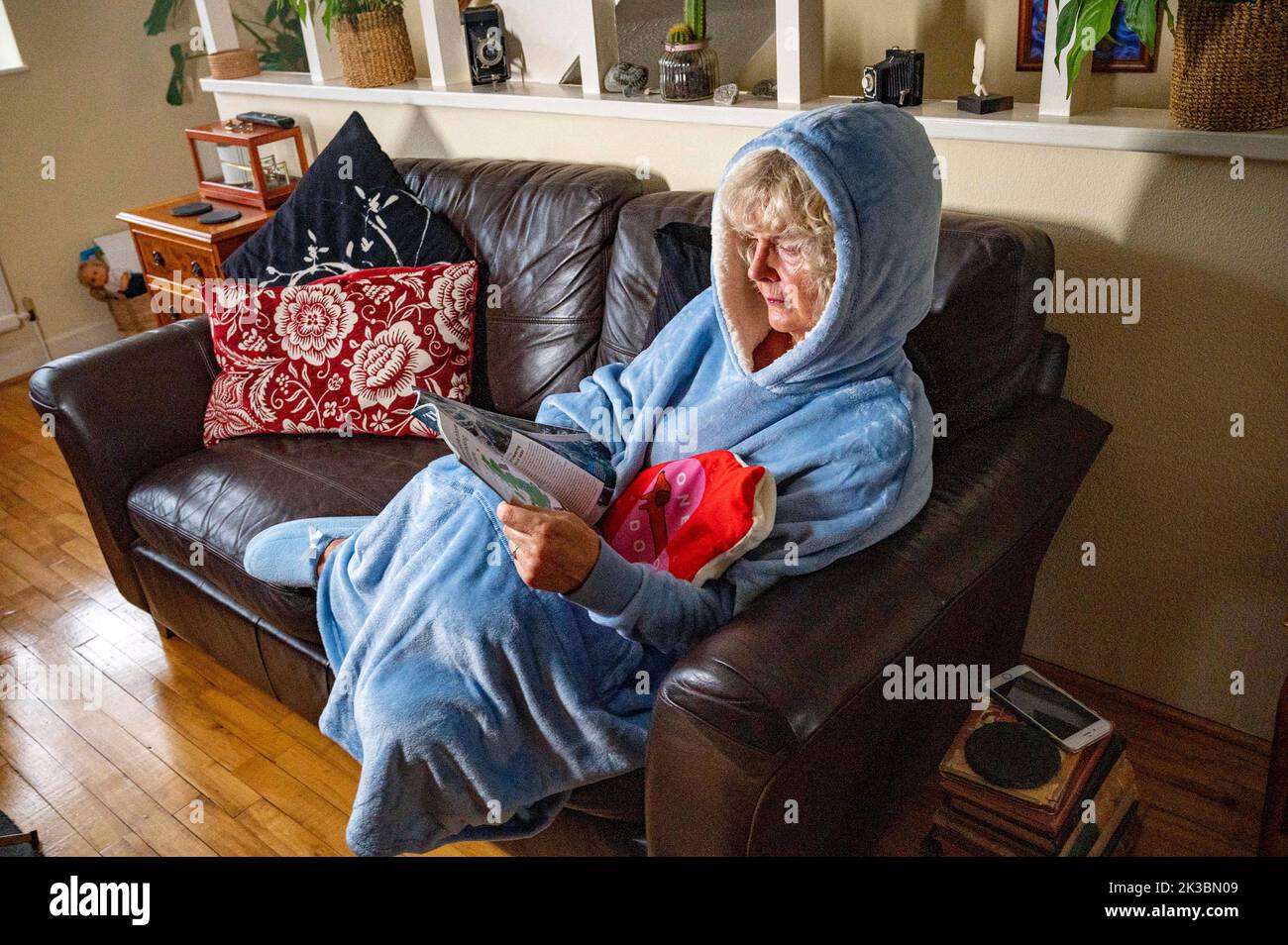 Femme portant une veste polaire avec capuche ou sweat à capuche et tenant une bouteille d'eau chaude pour rester au chaud à la maison car les coûts énergétiques sont à la hausse au Royaume-Uni (posé par le modèle) Banque D'Images