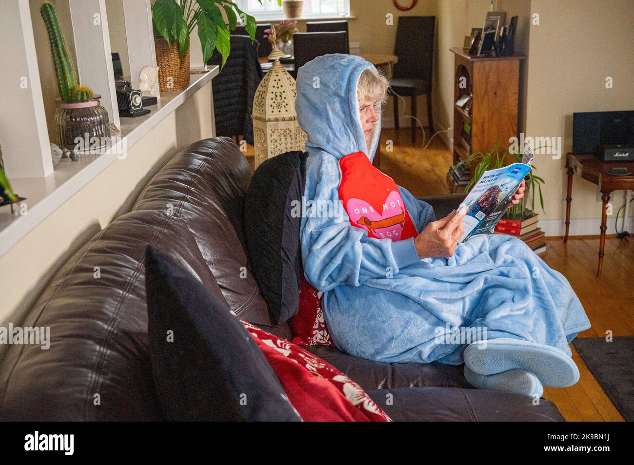 Femme portant une veste polaire avec capuche ou sweat à capuche et tenant une bouteille d'eau chaude pour rester au chaud à la maison car les coûts énergétiques sont à la hausse au Royaume-Uni (posé par le modèle) Banque D'Images
