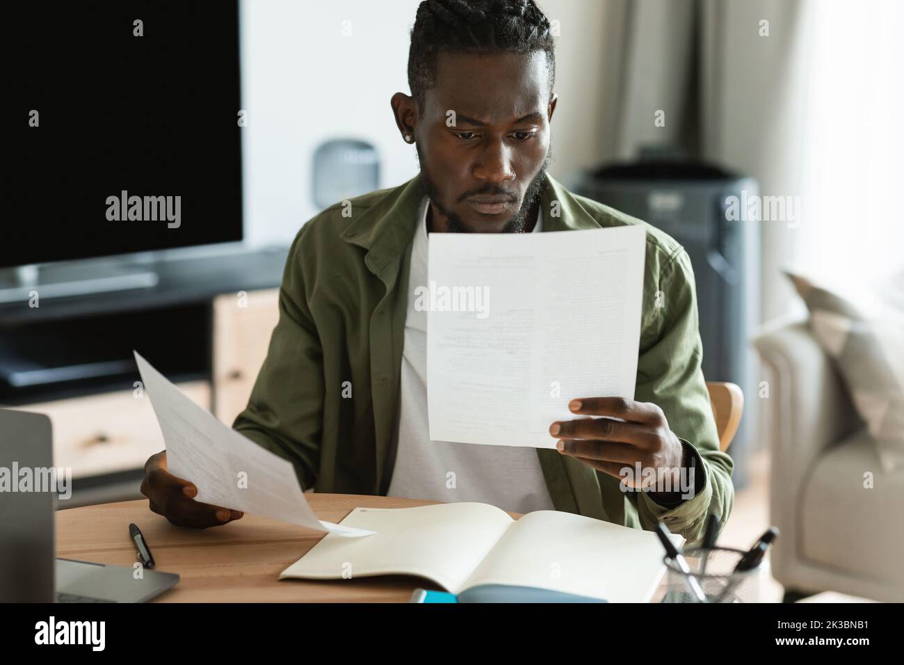 Homme afro-américain concentré de vérifier les documents, de calculer les factures et les taxes à l'aide d'un ordinateur portable dans l'intérieur de la chambre Banque D'Images