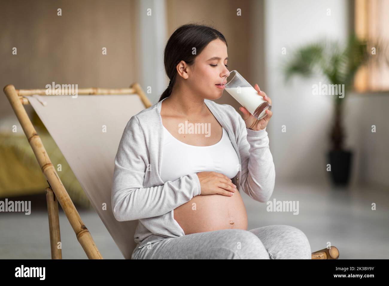 Femme enceinte boire du lait en verre tout en se relaxant sur la chaise à la maison Banque D'Images