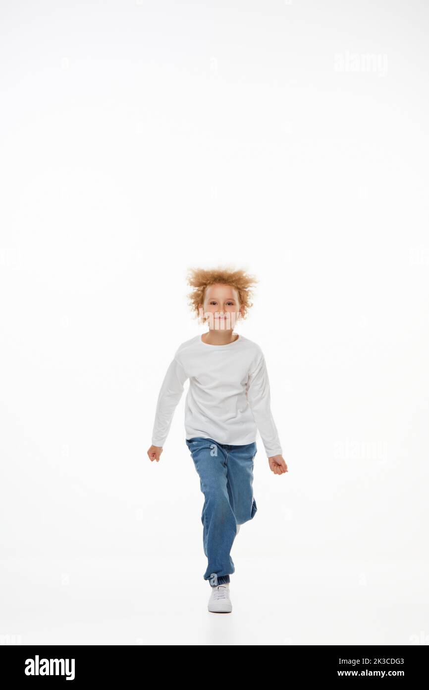 Portrait complet de petite fille, enfant en blouse blanche à manches longues et jeans isolés sur fond blanc. Mode, bonne enfance Banque D'Images