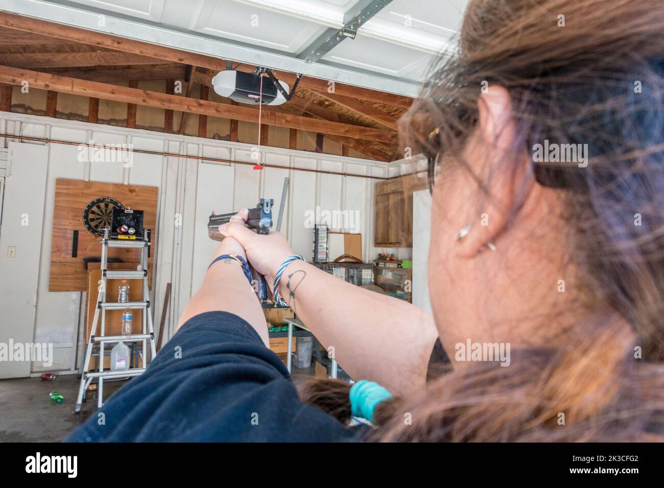 Vue sur l'épaule d'une femme visant et tirant un pistolet à air dans un garage. Banque D'Images