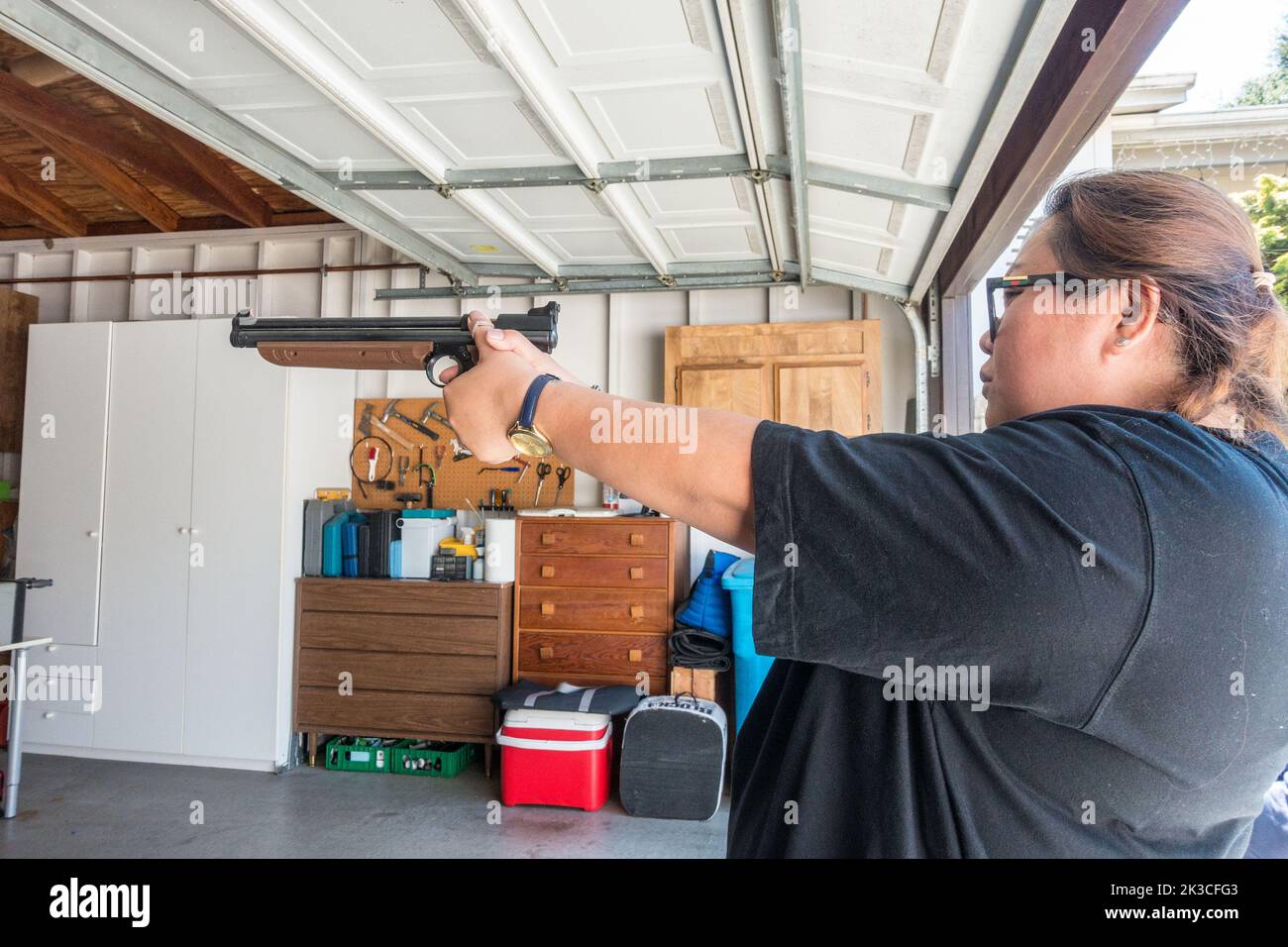 Une femme visant et tirant un pistolet à air dans un garage. Banque D'Images