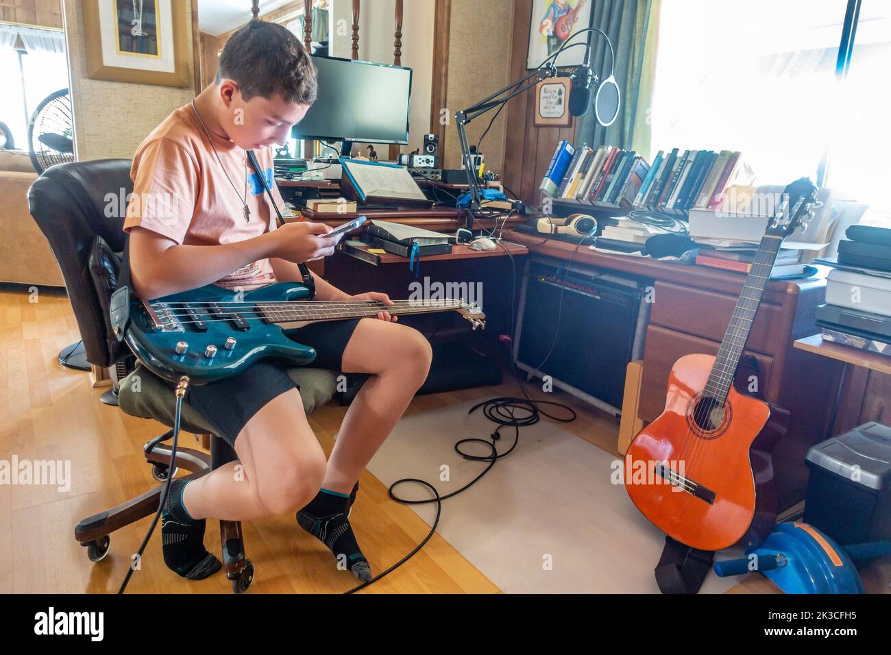 Un garçon auto-éduque en regardant une vidéo d'instruction sur un smartphone pour apprendre à jouer un morceau sur une guitare basse électrique Banque D'Images