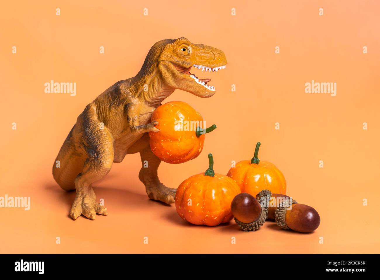 Jouet dinosaure Tyrannosaurus tenant la citrouille dans ses pattes, sur le podium blanc isolé sur fond orange carte de vœux de vacances Joyeux jour d'Halloween, Hello Autumn Creative minimal concept. Banque D'Images