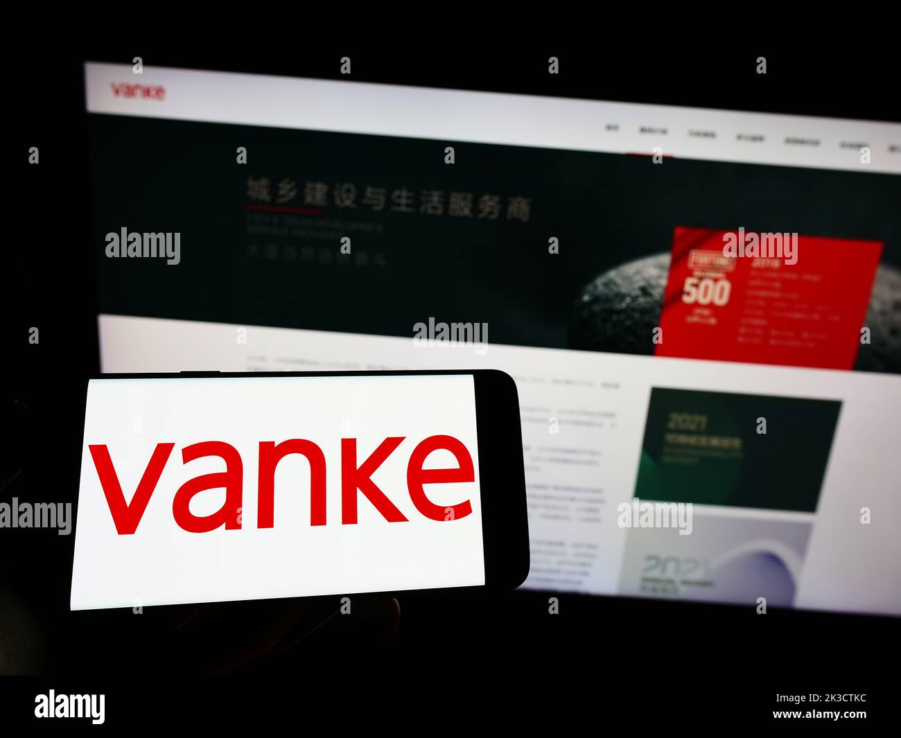 Personne tenant un téléphone portable avec le logo de la société immobilière chinoise Vanke Co. Ltd. À l'écran en face de la page Web d'affaires. Mise au point sur l'affichage du téléphone. Banque D'Images