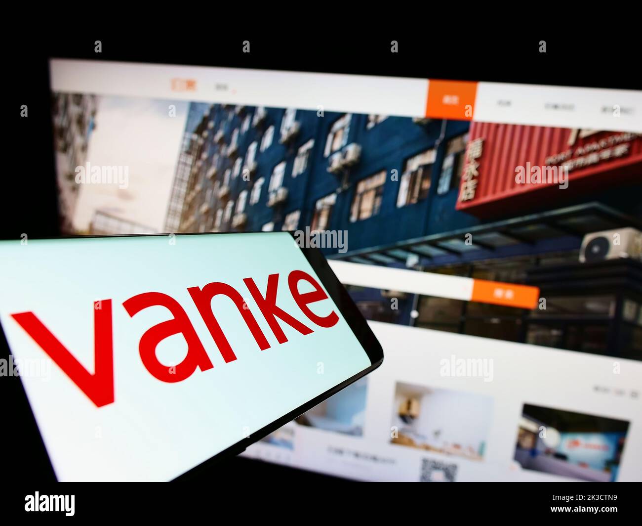 Téléphone portable avec logo de la société immobilière chinoise Vanke Co. Ltd. À l'écran devant le site Web d'affaires. Effectuez la mise au point à droite de l'écran du téléphone. Banque D'Images