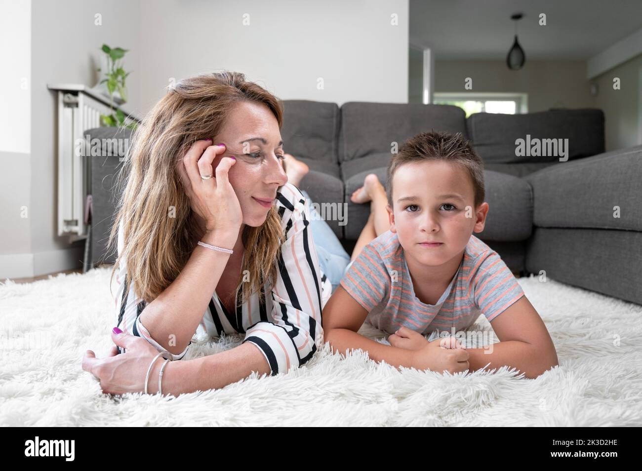 Fils et mère couchés ensemble sur un tapis blanc. Photographie de haute qualité Banque D'Images