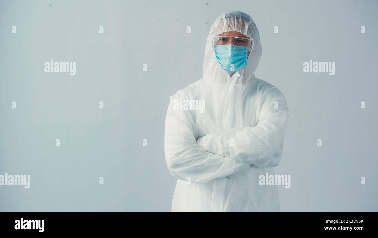 médecin en costume de noisette et masque médical avec des lunettes debout avec des bras croisés sur fond gris, image de stock Banque D'Images