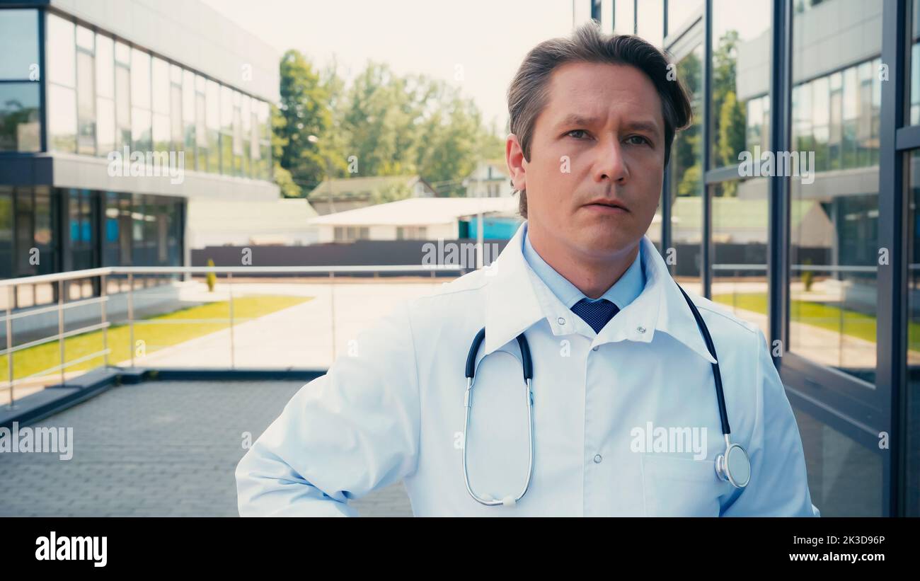 docteur en manteau blanc et avec stéthoscope regardant loin près de l'hôpital de ville, image de stock Banque D'Images