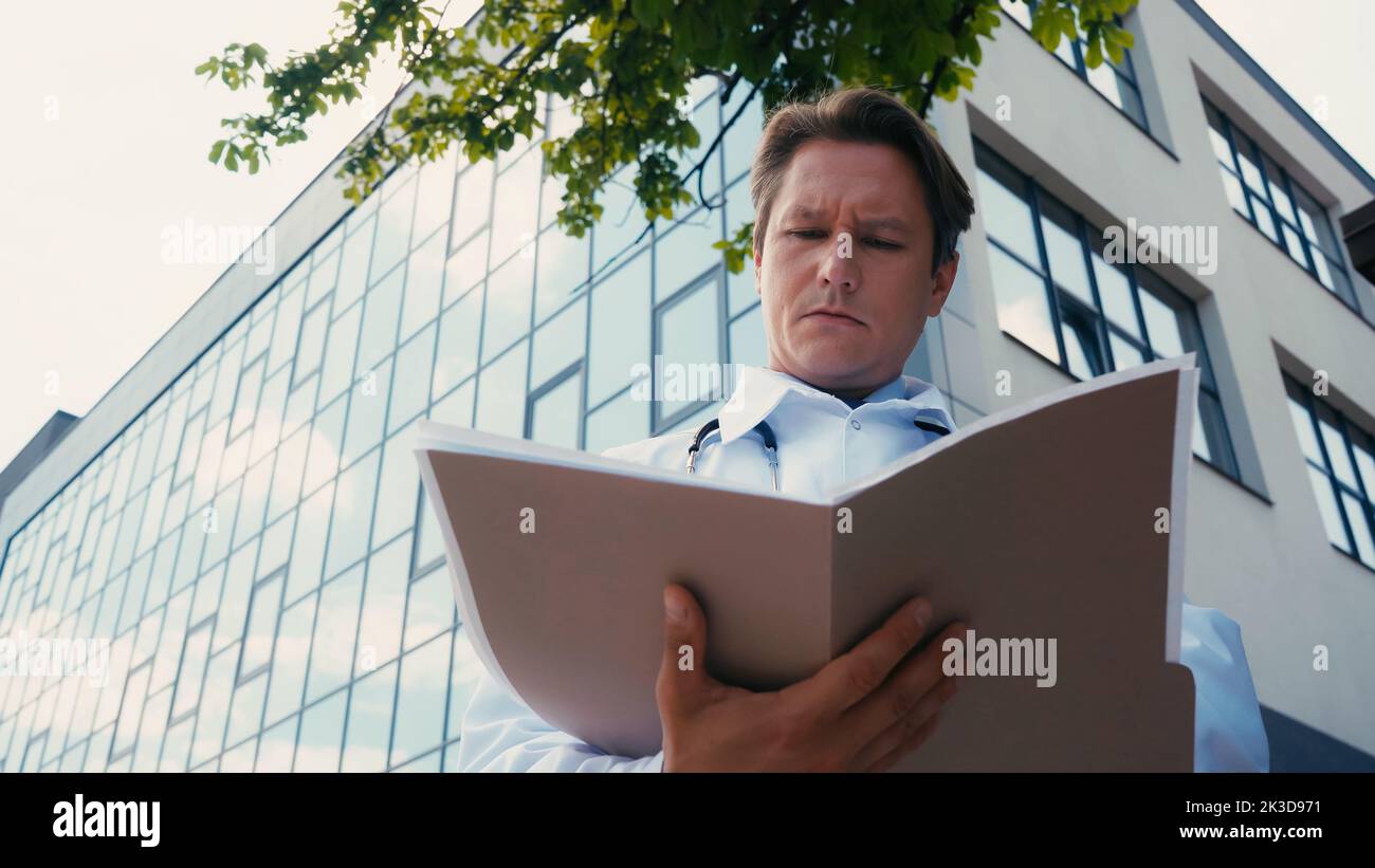 vue à angle bas du médecin regardant dans le dossier avec des documents près du bâtiment de l'hôpital, image de stock Banque D'Images