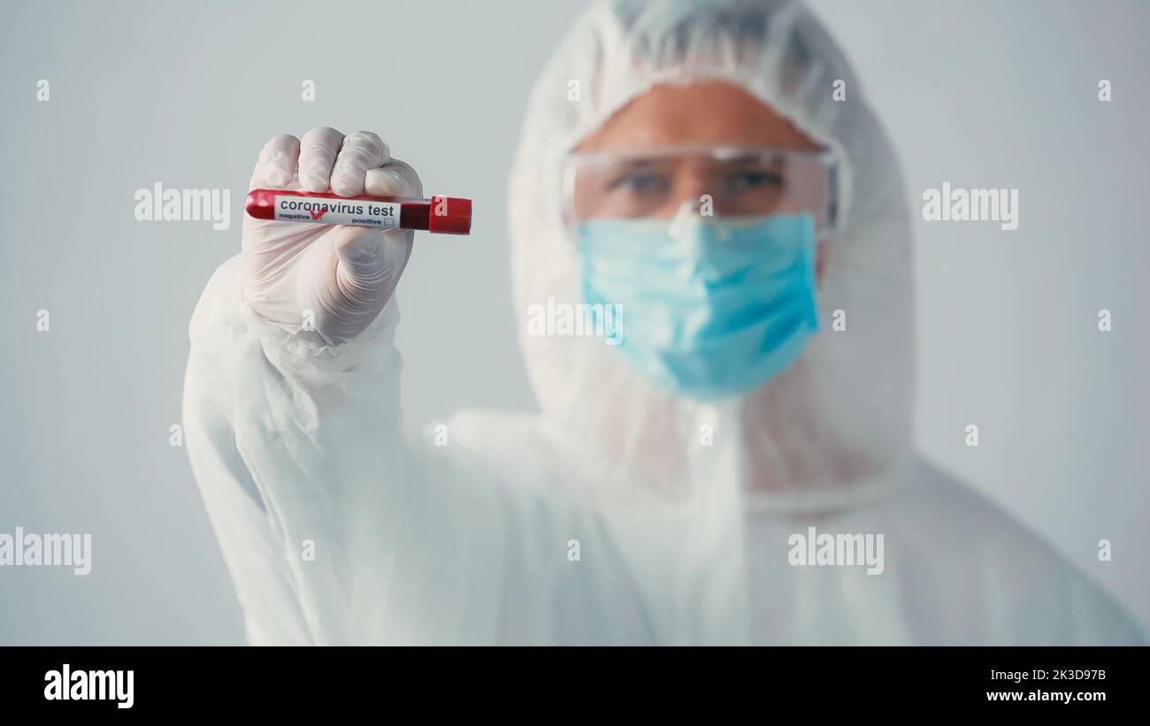 médecin flou en costume de noisette montrant le test négatif du coronavirus isolé sur image grise, stock Banque D'Images