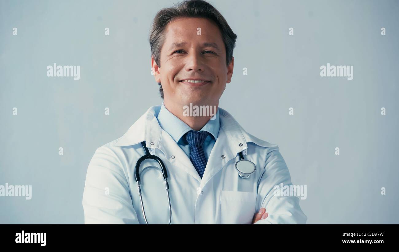 joyeux médecin en manteau blanc souriant à la caméra isolée sur gris, image de stock Banque D'Images