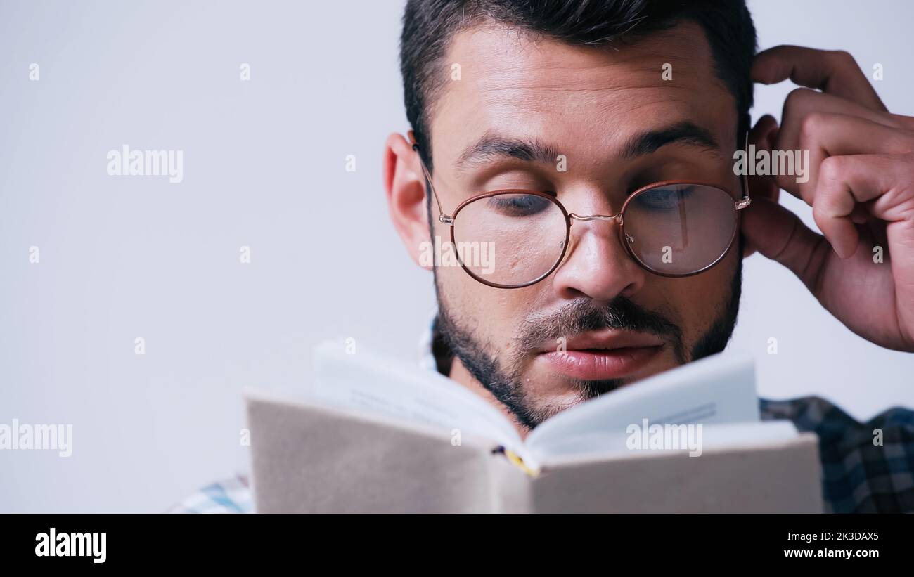 pensive nerd étudiant en lunettes de lecture livre flou et touchant la tête isolée sur gris, image de stock Banque D'Images
