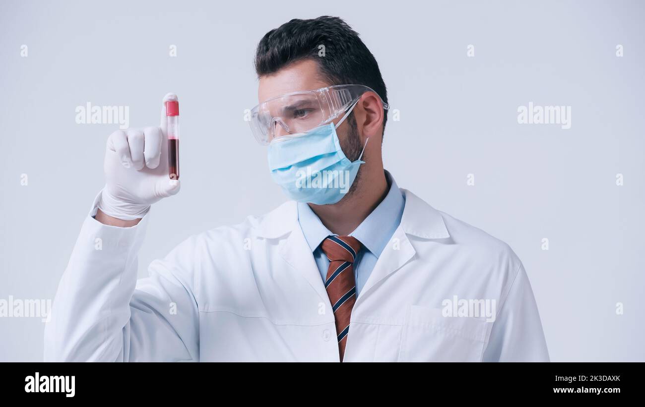 immunologiste dans un masque médical et des lunettes de protection regardant le tube à essai avec un échantillon de sang isolé sur une image grise du stock Banque D'Images