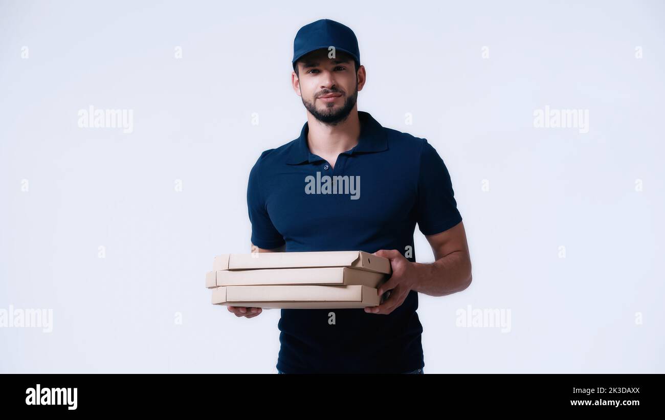 jeune livreur en uniforme bleu tenant des boîtes à pizza et regardant la caméra isolée sur blanc, image de stock Banque D'Images