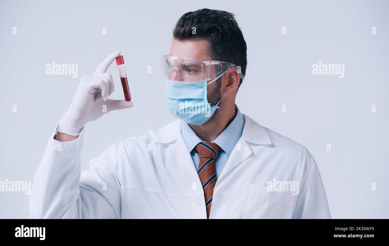 brunette médecin en masque médical et gant de latex tenant le tube à essai avec le sang isolé sur gris, image de stock Banque D'Images